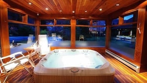 Una cabaña de madera con jacuzzi, ventanas amplias y vistas al exterior.
