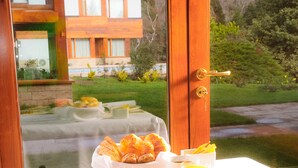 Una mesa de desayuno con diversos platos, entre ellos huevos, tostadas y fruta, con vistas a una casa y vegetación.