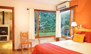 Un dormitorio con cama, sillón, ventana con vistas a follaje y chimenea.