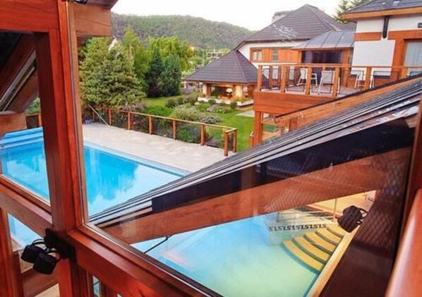 A view from a balcony with a pool, wooden deck, and a house in the background.