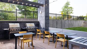 Un patio exterior con una parrilla, mesas y sillas.