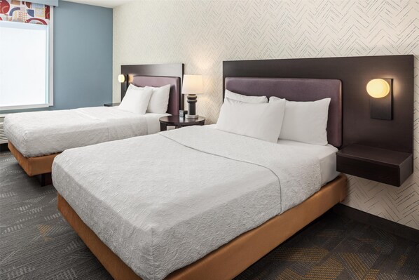 Habitación de hotel con dos camas, cada una con cabecera y mesita de noche, y un ventanal grande.