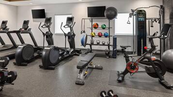 Ein Fitnessstudio mit Laufbändern, Crosstrainern, einer Bank, Kurzhanteln, einem Gewichtständer und einem Ergometer.