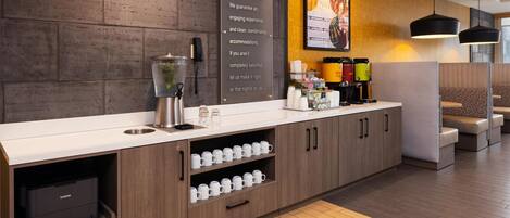 A modern hotel reception area with a wooden counter, a coffee machine, and a sign stating "HOME2 GUARANTEE".