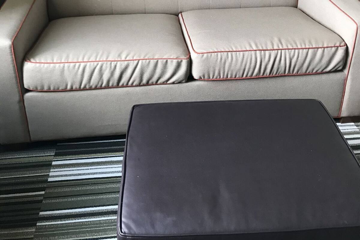 Un sofá color beige con detalles rojos, un reposapiés negro y una vista panorámica de la ciudad a través de una ventana.