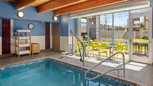 An indoor swimming pool with clear blue water, a wooden ceiling, and a view of an outdoor patio with yellow chairs and tables. - Home2 Suites by Hilton Roseville Minneapolis (Roseville)