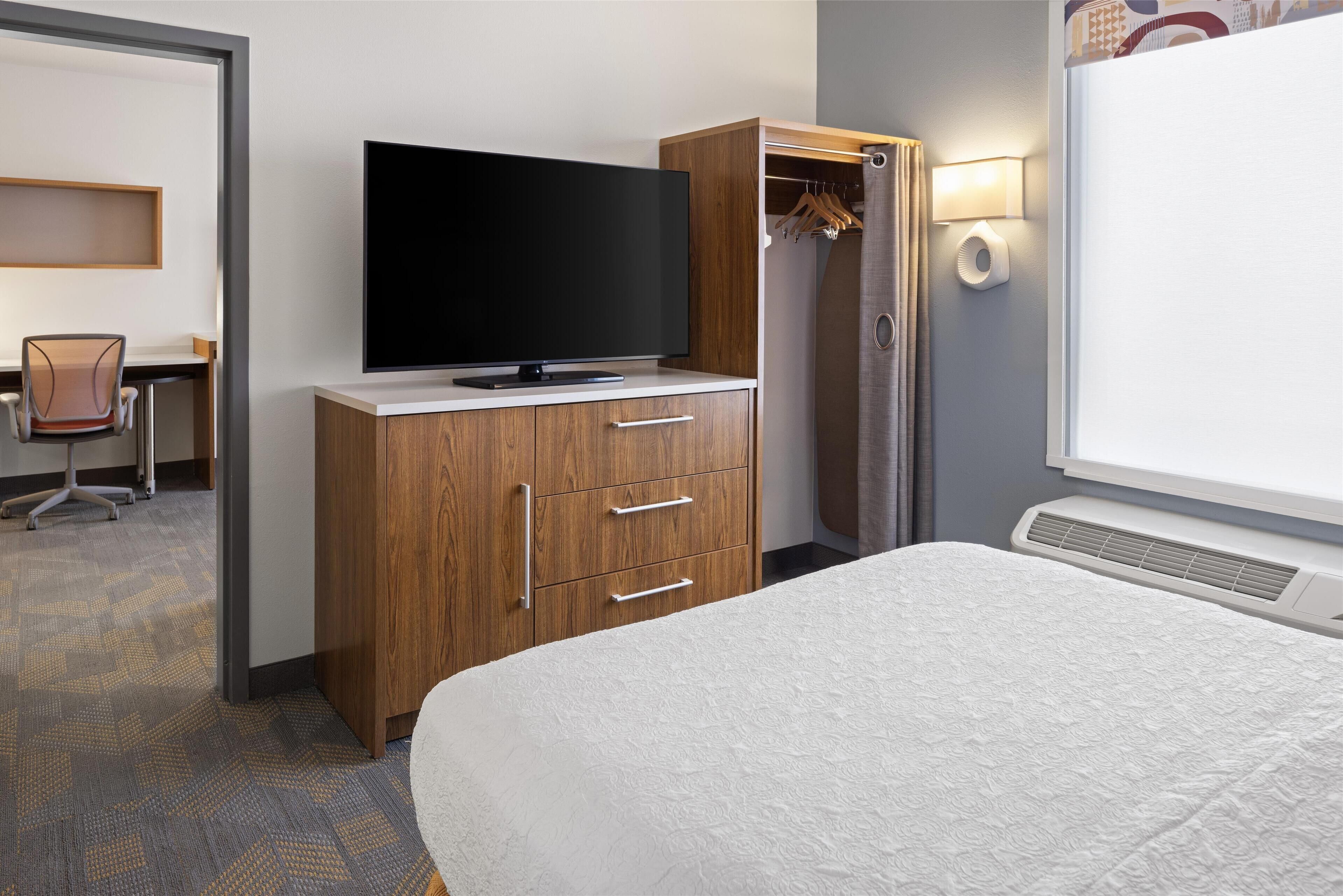 Ein Hotelzimmer mit einem Bett, einem Fernseher auf einer Holzkommode, einem Schreibtisch mit Stuhl und einem Kleiderschrank.