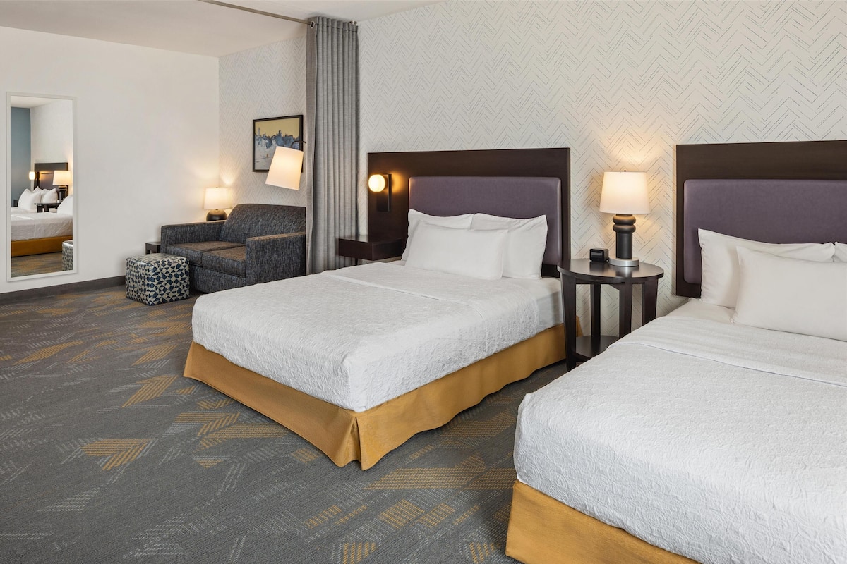A hotel room with two beds, a sofa, a mirror, and a lamp.