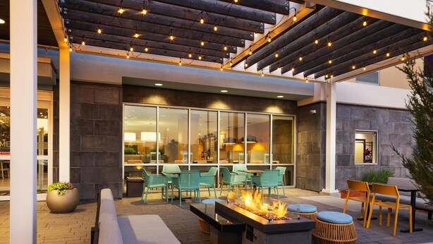 An outdoor patio with a fire feature, seating, and a covered area with string lights. - Home2 Suites by Hilton Roseville Minneapolis (Roseville)