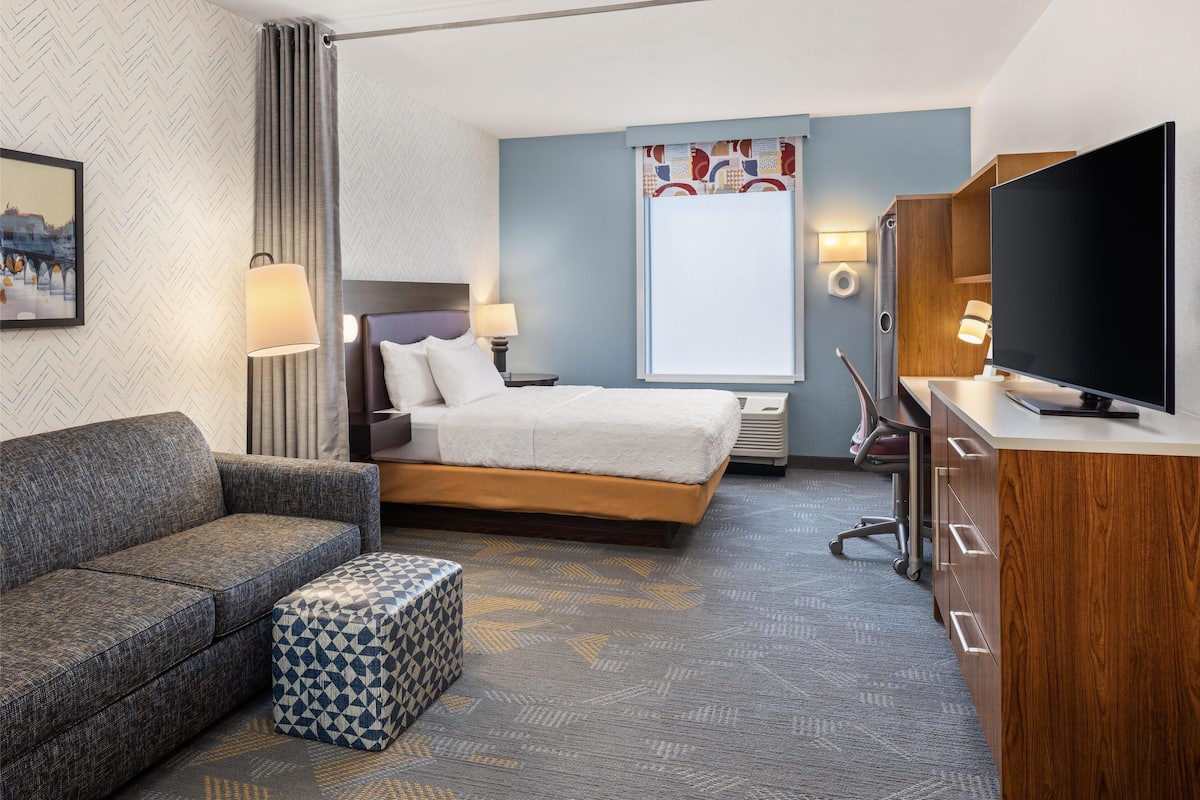 A hotel room with a bed, a sofa, a TV, and a desk.