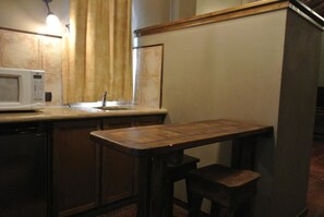 Een kleine keuken met een magnetron, een spoelbak en een houten tafel met een kruk.