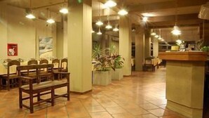A spacious dining area with wooden chairs and tables, a reception desk, and hanging pendant lights. - Aire Andino Apart Hotel (San Juan)