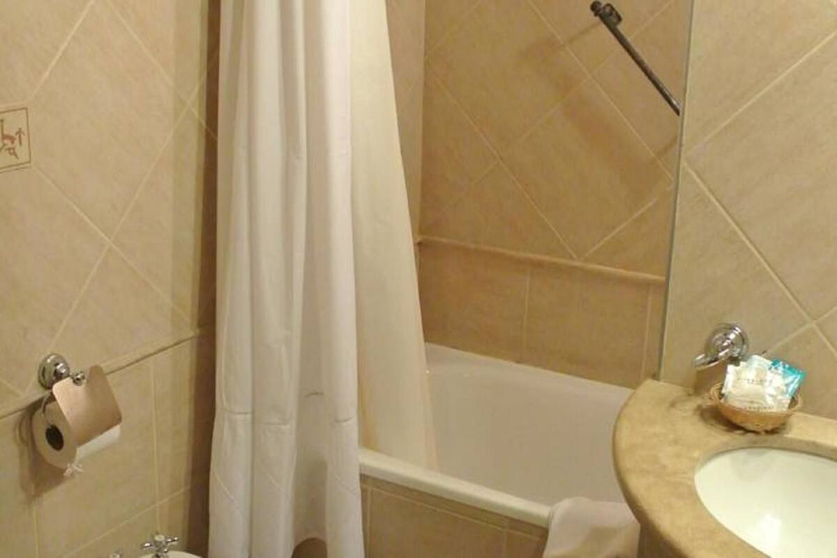 Un bagno con piastrelle beige, un water, una tenda da doccia, una vasca e un lavandino con articoli da toilette.