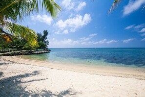 A beach with clear turquoise water, white sand, and palm trees. - Bayside Villa 3A (Roatan)