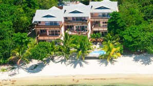 A beachfront property with multiple buildings, a swimming pool, and palm trees. - Bayside Villa 3A (Roatan)