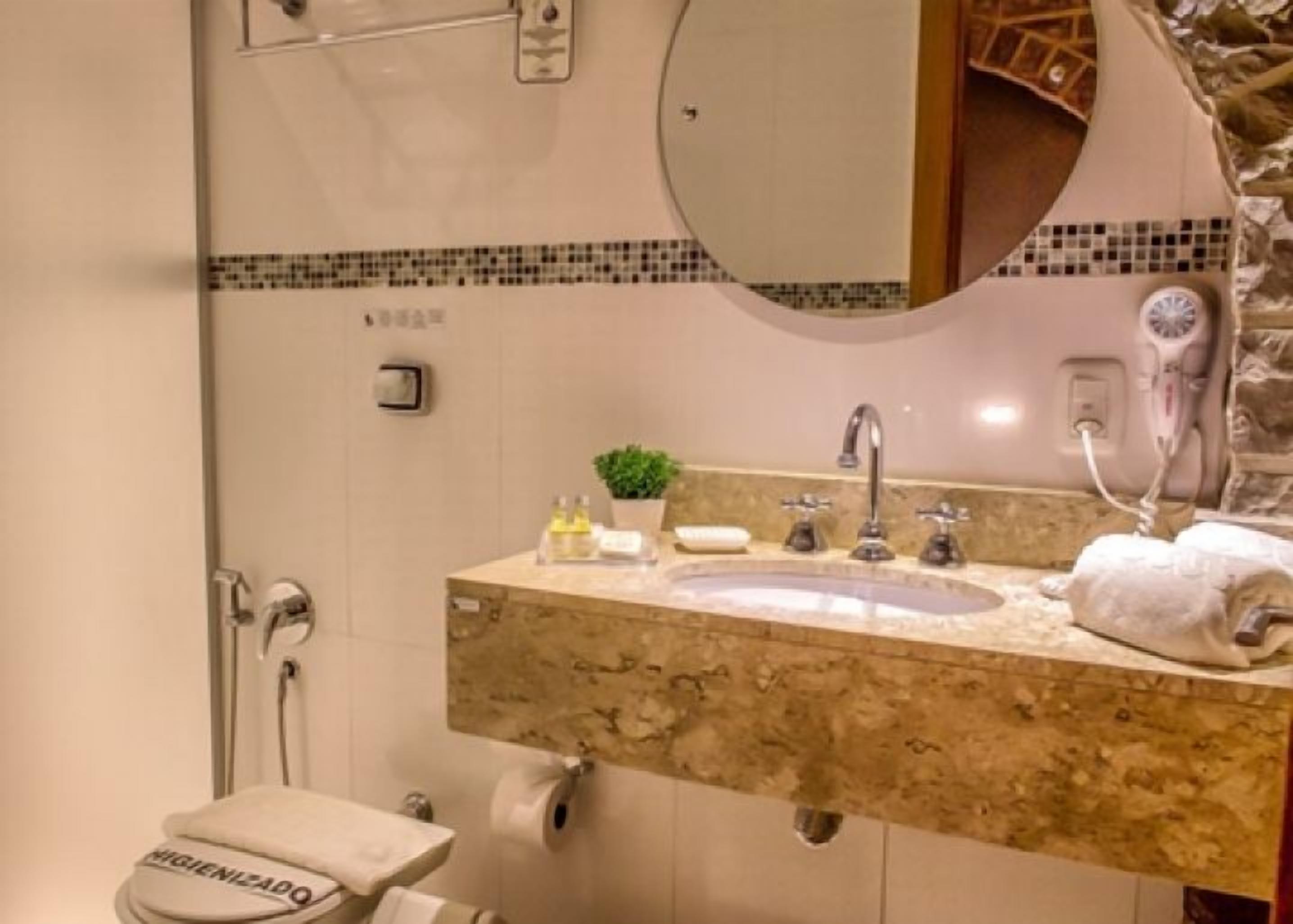 A bathroom with a marble sink, a mirror, a hairdryer, and a towel.