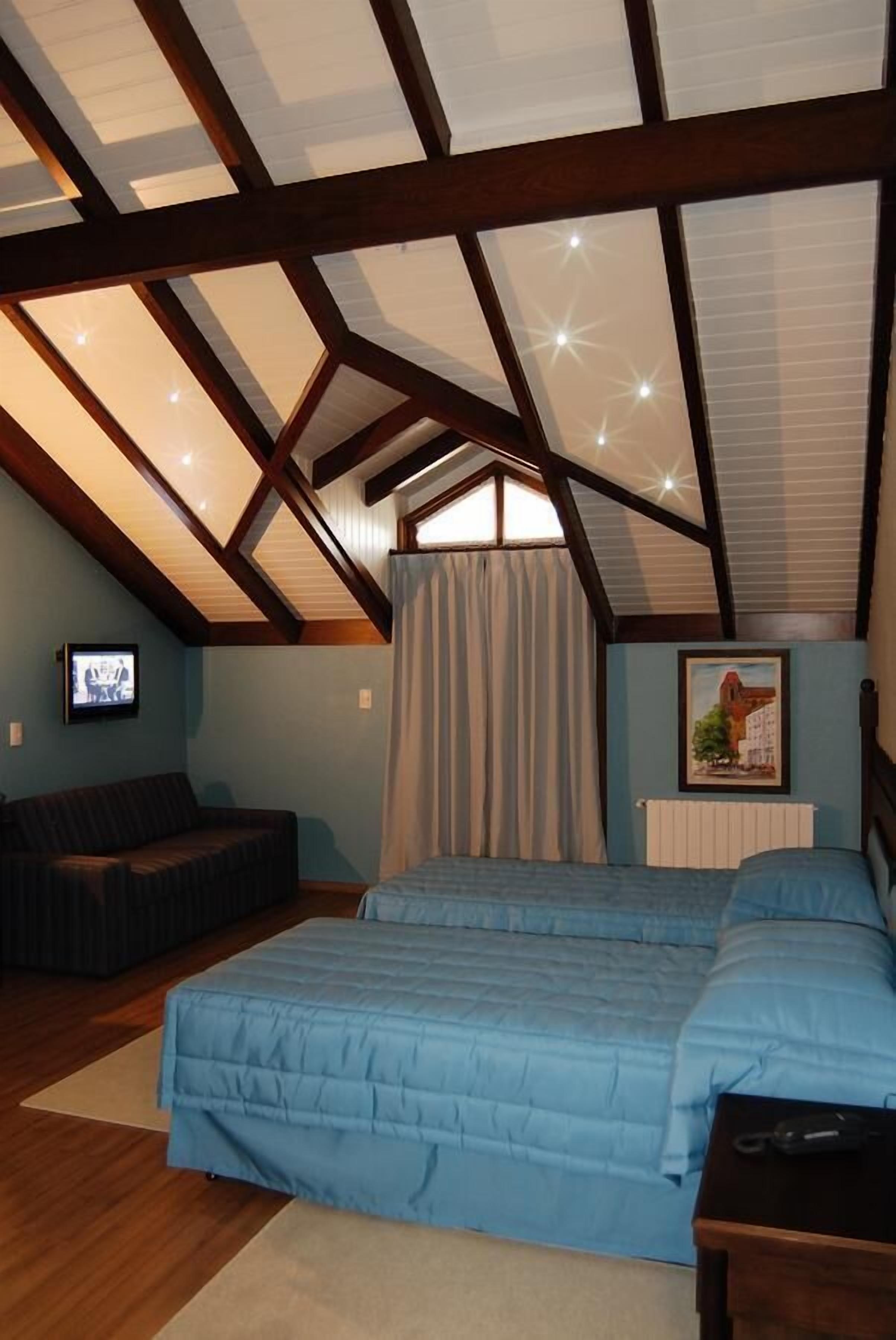Ein Schlafzimmer mit schrägem Dach, einem Bett, einer Couch, einem Fernseher und einem Bild an der Wand.