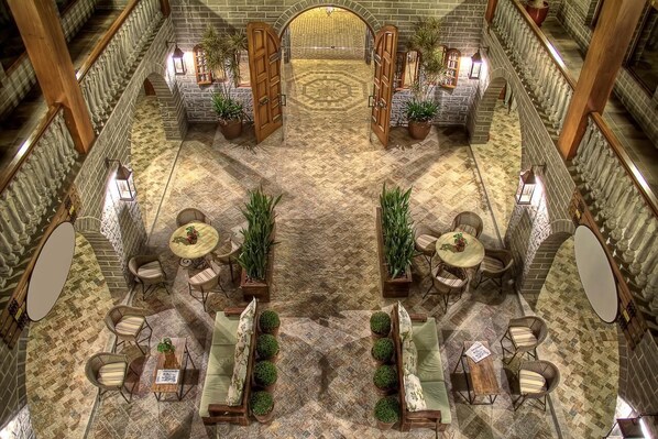 A spacious indoor area with a central open space surrounded by seating arrangements and potted plants. - Pousada Castello Benvenutti (Garibaldi)