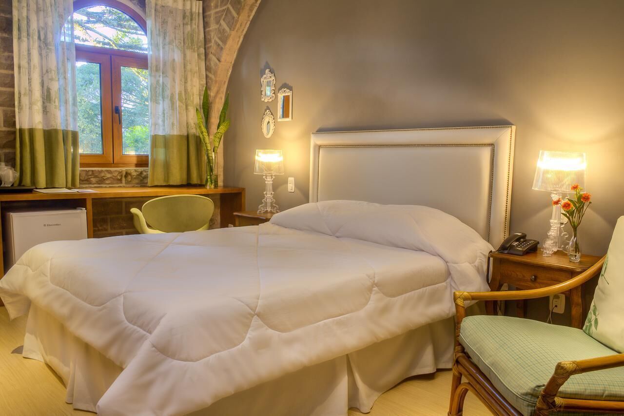 Una habitación de hotel con una cama grande, un escritorio con computadora, una silla y una lámpara.