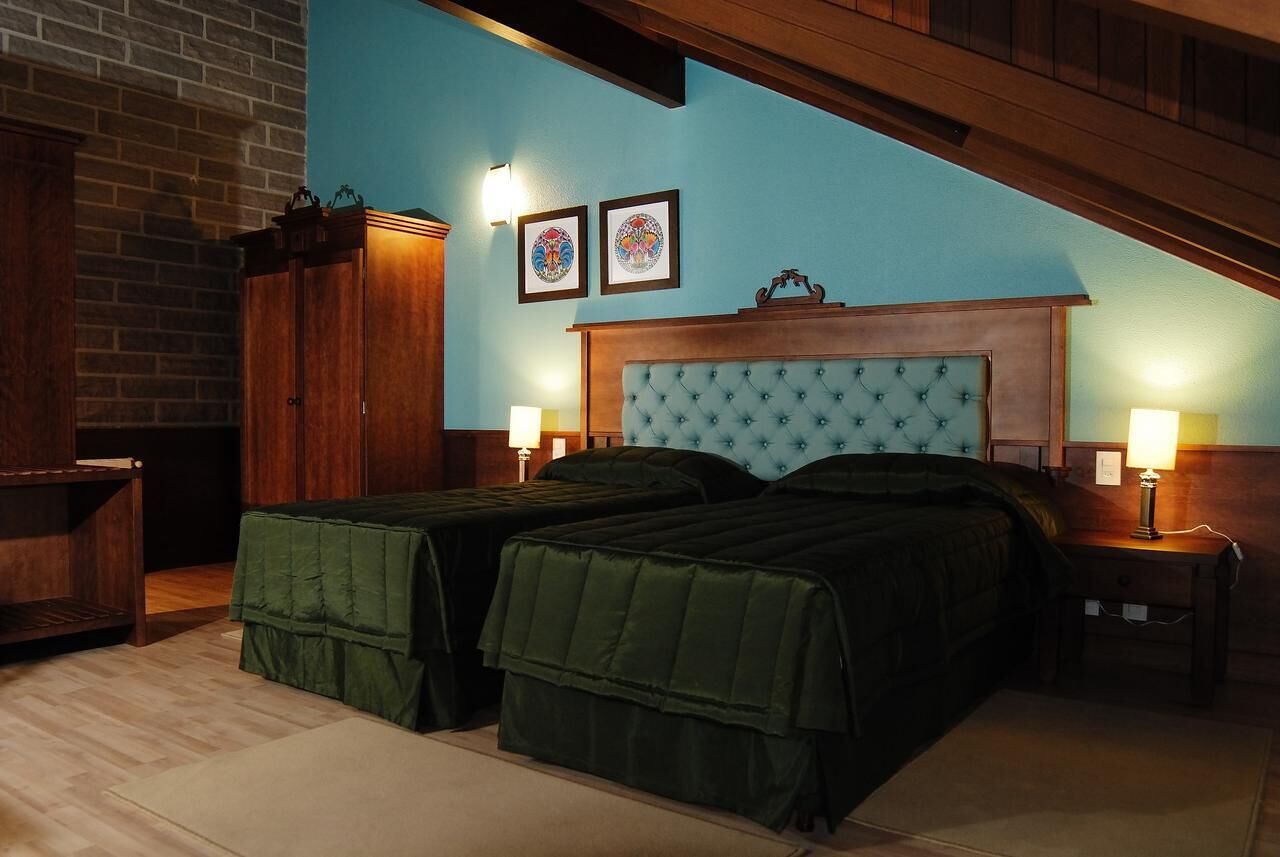 Una habitación con dos camas, cabecero de madera, pared de ladrillo y dos cuadros enmarcados.