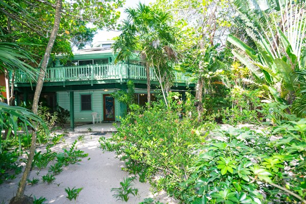A lush garden with a green building featuring a balcony, surrounded by dense tropical foliage.