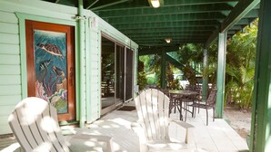 A covered outdoor seating area with Adirondack chairs and a table, a mural of sea life on the wall, and a covered entrance. - Playa Bonita 1 bedroom (Roatan)