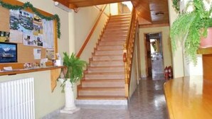 Zona de recepción con una escalera de madera, un tablón de anuncios con varios avisos y un mostrador de recepción.