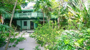 Um jardim exuberante com um edifício verde e varanda, rodeado por vegetação tropical densa.