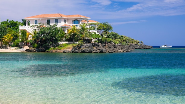 A coastal property with a white building featuring a red-tiled roof, surrounded by lush greenery and a clear blue sea. - Coral Vista 1 (Roatan)