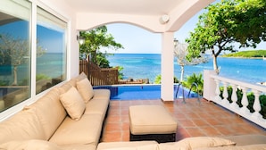 A balcony with a beige sofa, a small table, and a view of the sea. - Coral Vista 1 (Roatan)