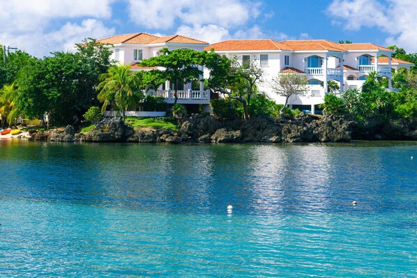 A beachfront property with multiple white buildings, a clear blue sea, and lush greenery.