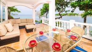 A terrace with a glass table surrounded by wicker chairs, a beige sofa, and a view of the sea. - Coral Vista 1 (Roatan)