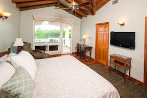 A bedroom with a bed, a television, a ceiling fan, a window with a view, and a door.