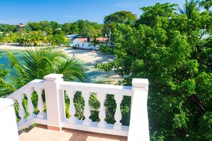 A balcony with a white balustrade overlooking a beach with palm trees and a clear blue sky.