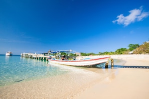 A beach with clear water, a pier, and boats.