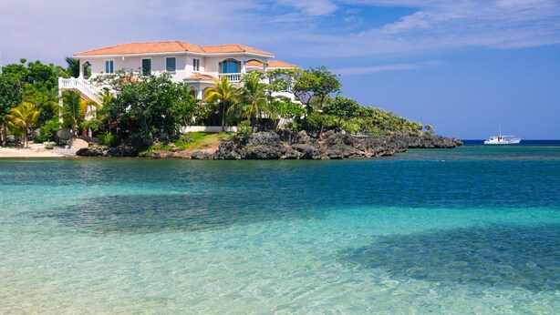 A coastal property with a white building featuring a red-tiled roof, surrounded by lush greenery and a clear blue sea. - Coral Vista 1 2 bedroom option (Roatan)