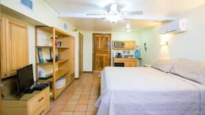 A bedroom with a bed, a desk with a computer, a wardrobe, a microwave, and a ceiling fan. - Playa Bonita Studio (Roatan)