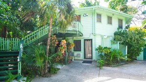 A light green house with a balcony, surrounded by lush greenery and a concrete driveway. - Playa Bonita Studio (Roatan)