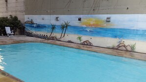 Une piscine ornée d’une fresque représentant une scène de plage, avec des palmiers et un coucher de soleil.