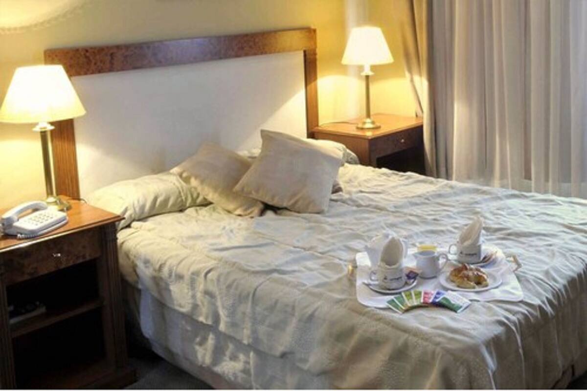 Habitación de hotel con cama, dos mesitas de noche, lámparas, teléfono y bandeja para el desayuno.