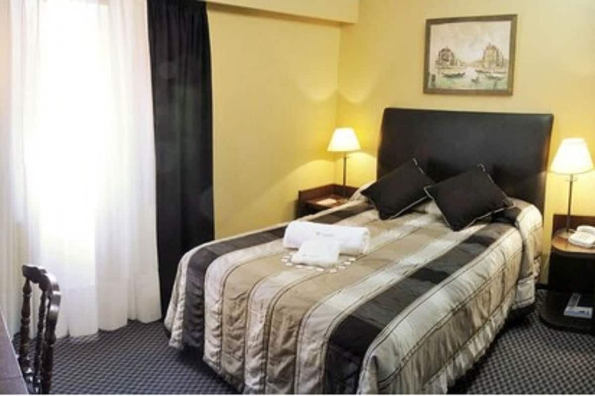 Una habitación de hotel con una cama, lámparas de noche, un televisor y un cuadro en la pared.