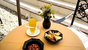 Taula amb una beguda, un bol de fruits secs i un bol de patates cruixents, col·locada a l'aire lliure amb una piscina i un edifici al fons.