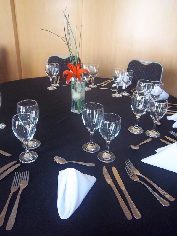 Una mesa lista para comer, con copas de vino, cubiertos y un florero con flores.
