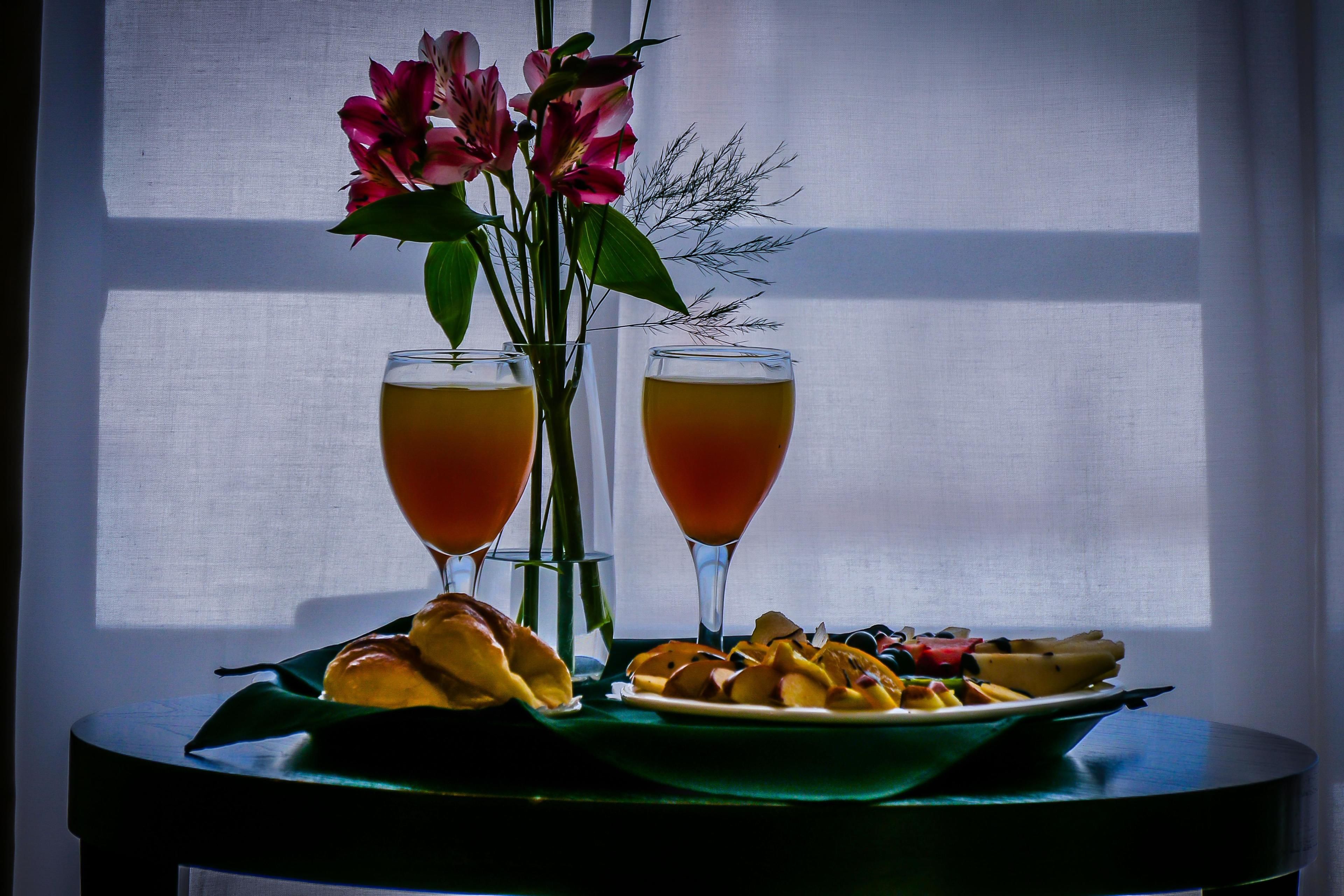 A table with two glasses of a beverage, a plate of fruit, and a vase with flowers.