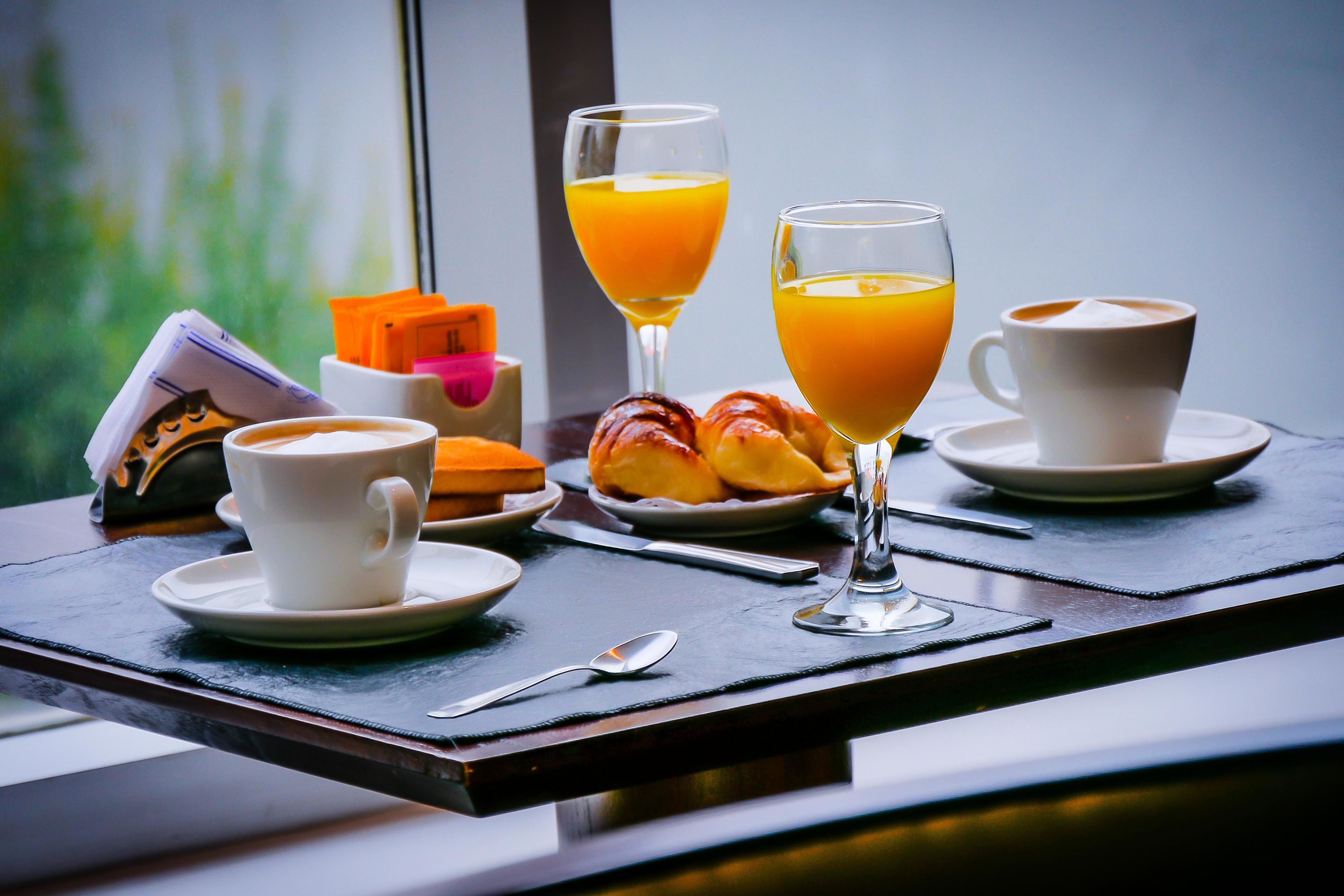 A breakfast setting with croissants, orange juice, and coffee on a table near a window.