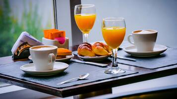 A breakfast setting with croissants, orange juice, and coffee on a table near a window.