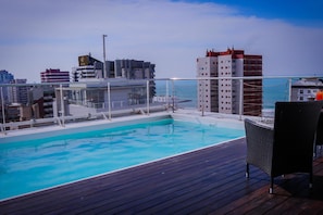 Ein Pool auf dem Dach mit einer Holzterrasse und Gartenmöbeln, umgeben von Stadtgebäuden.