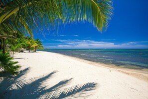 A beach with white sand, clear blue water, and palm trees under a bright sky.