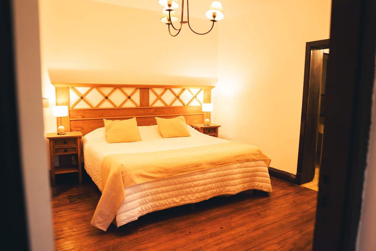 A neatly made bed with a wooden headboard, two bedside lamps, and a chandelier.