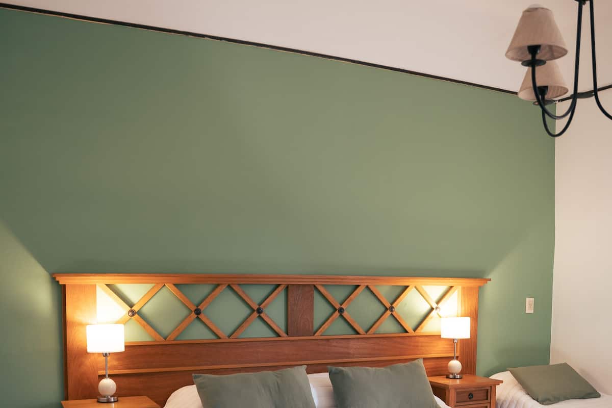 A bedroom with a wooden headboard, two bedside tables with lamps, a large bed with a green throw, and a hanging light fixture.